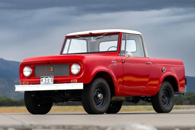 Red International Harvester Scout 80 truck parked on a road with cloudy skies behind it