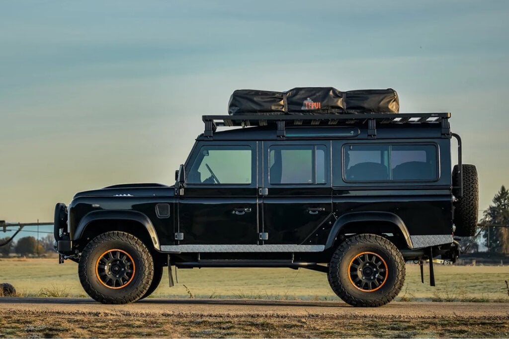 Side profile of a black Land Rover Defender on a dirt road with grass behind it