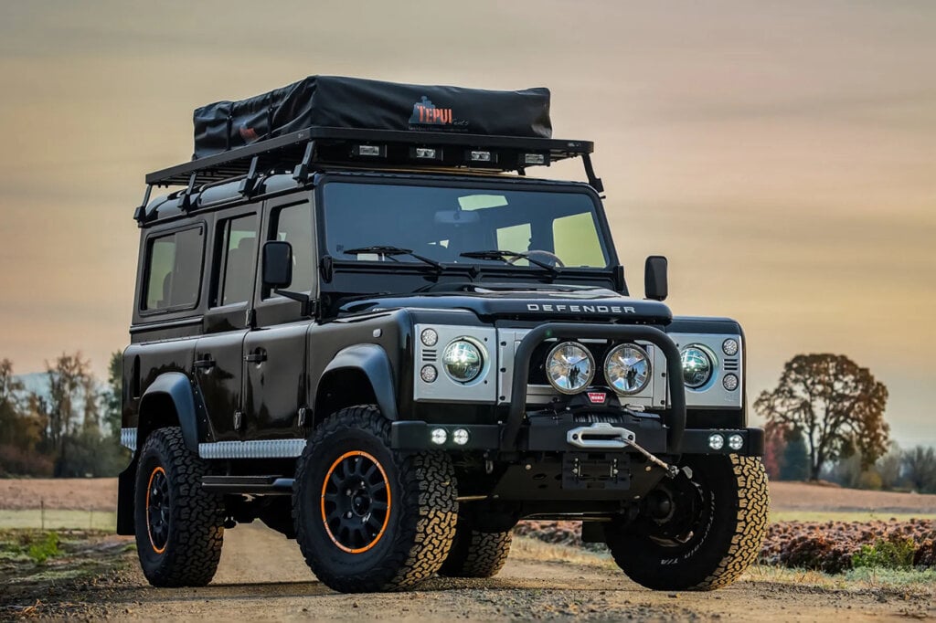 Black Land Rover Defender with overlanding gear parked on a dirt road