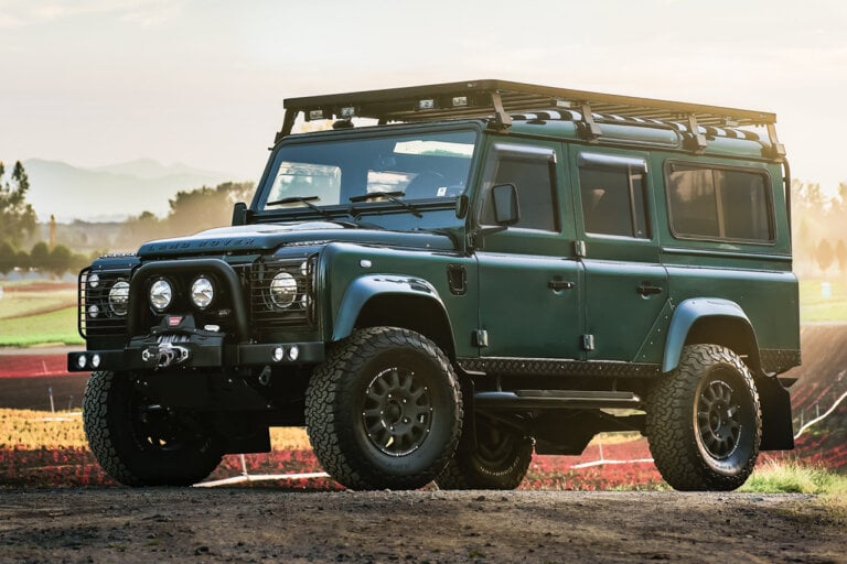Green Land Rover Defender parked at an angle with the sun setting in background