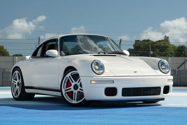 White Porsche RUF SCR parked on a blue floor with blue sky with clouds in background