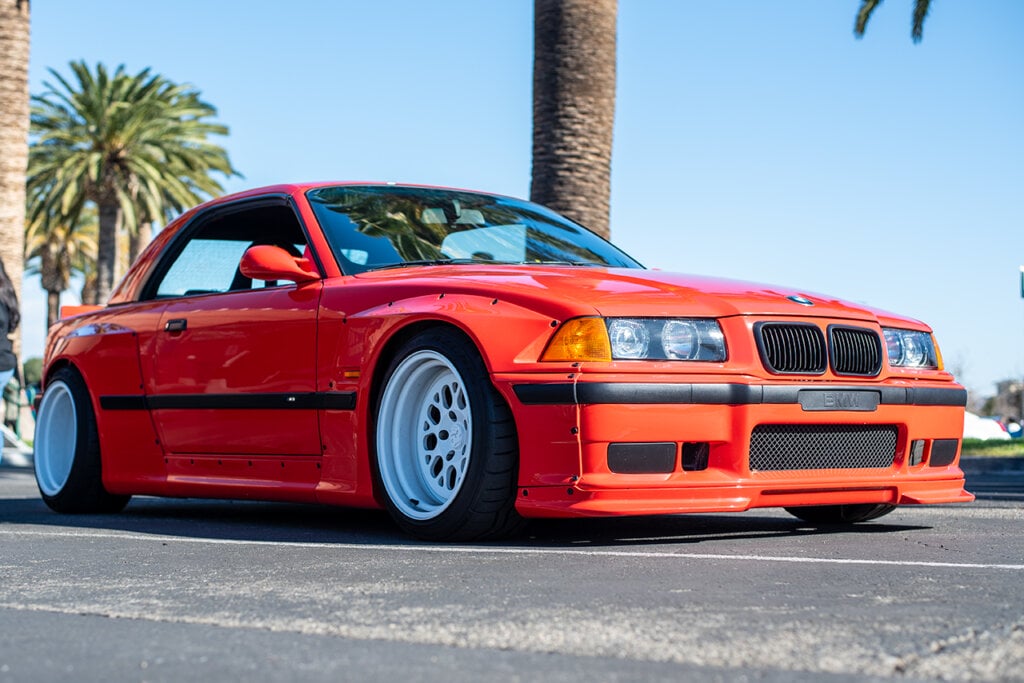 red BMW E36 M3 with white wheels and parked infront of a palm tree