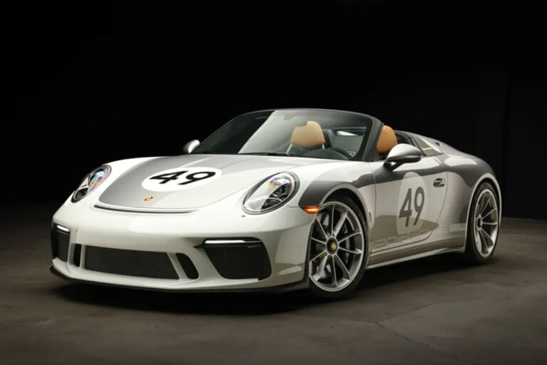 Silver Porsche 911 with the number 49 in a white circle. Car in a dark room with black background