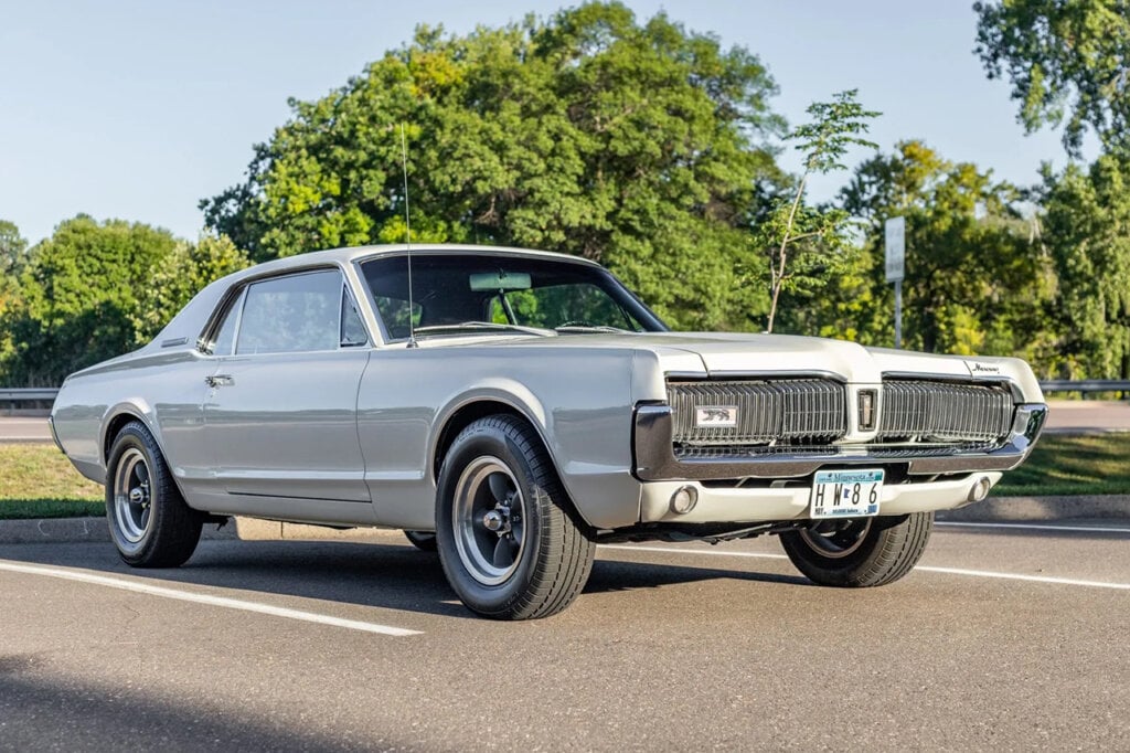 White Mercury Cougar parked in a parking lot near some trees