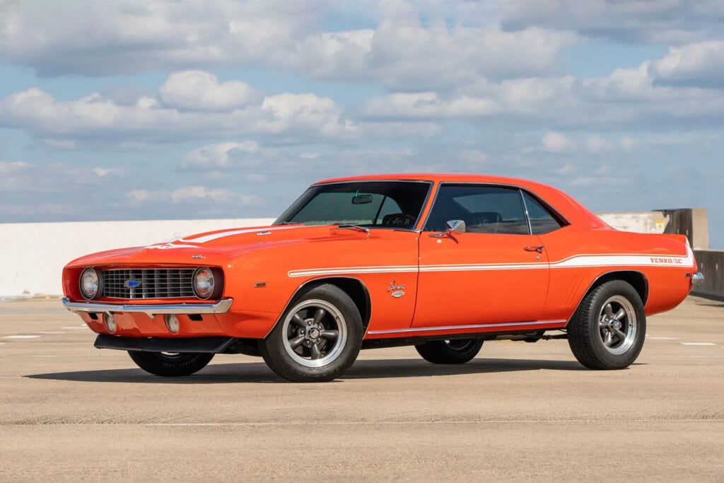Orange Chevrolet Camaro with white racing stripe and blue sky in background