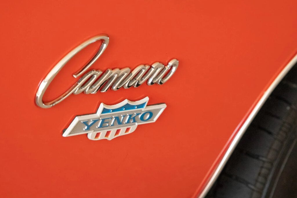 The word Camaro in a think font above the Chevrolet logo on an orange Camaro