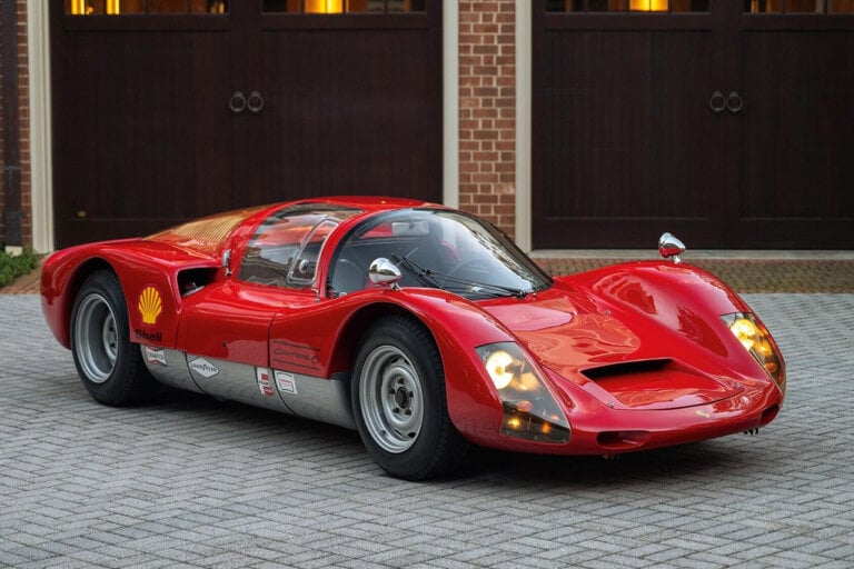 red Porsche 906 parked in a driveway in front of a garage