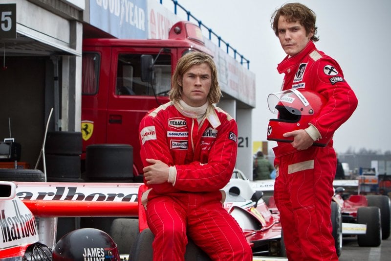 Two men in red race suits standing next to a race car, Chris Hemsworth and Daniel Bruhl
