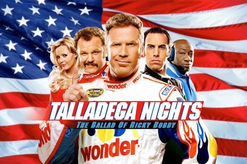 group of people standing infront of the American Flag. Man in the middle has is index finger pointing up with Talledega Nights movie title in front of them
