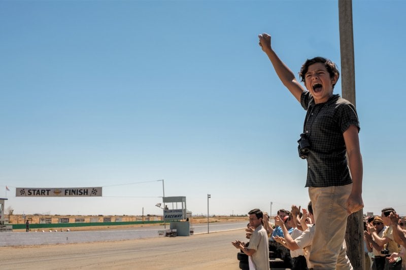 Boy raising his hand with a closed fist showing excitement in front of a crowd of spectators near a race track