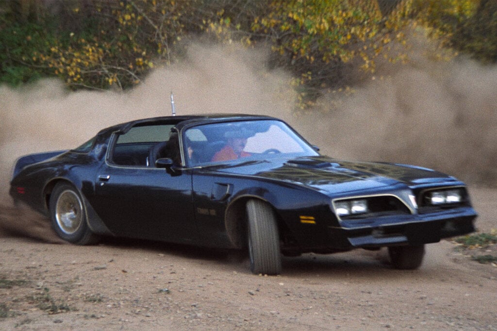 Actor Burt Reynolds behind the wheel of a black trans am going through a turn on the dirt