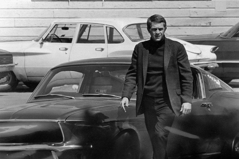 black and white photo of man next to a car walking away from it