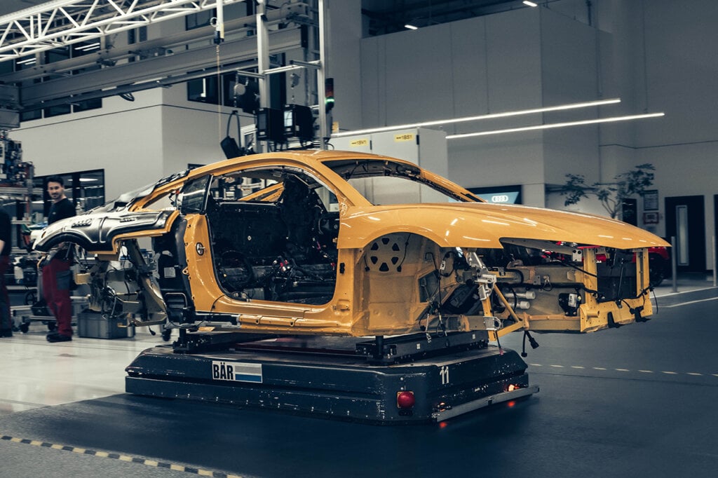 yellow car with exposed panels on a production line