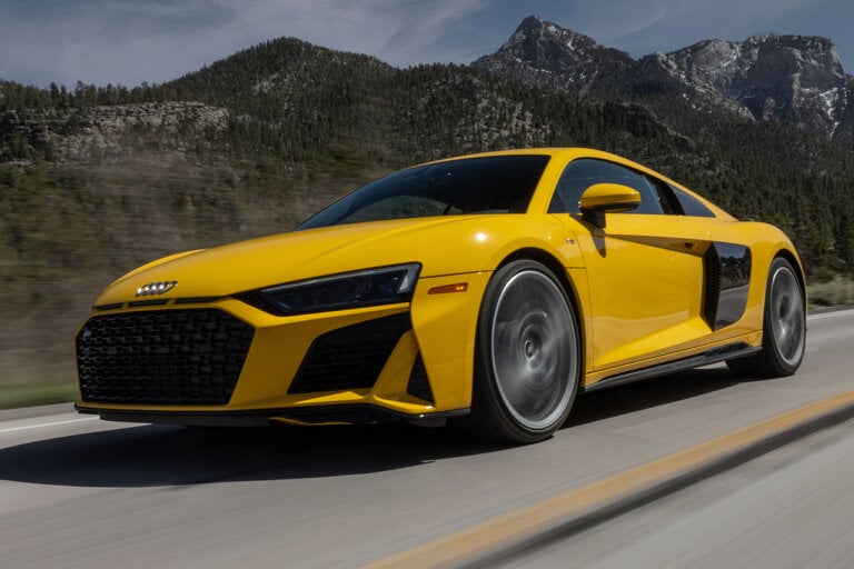 yellow audi R8 driving fast on road with mountains in background