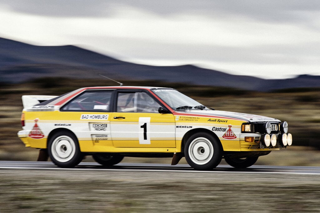 Yellow Audi quattro driving fast through the open landscape with mountains in background