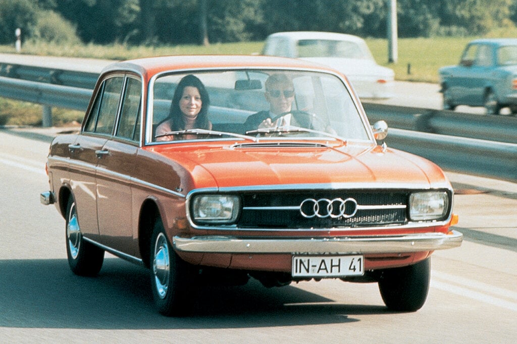Orange Audi F103 vehicle with man and woman driving it on a freeway