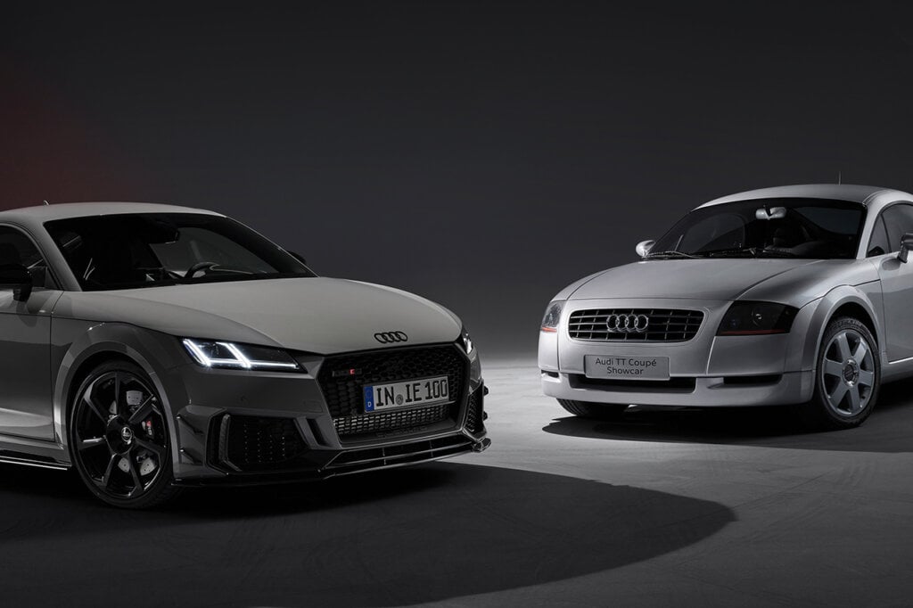 Two generations of grey Audi TT's parked on a dark background