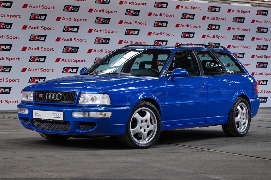 Blue RS2 parked in a warehouse with Audi branding on a background behind it