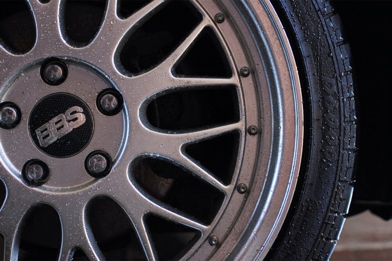 Silver wheel closeup with water droplets on it and the tire