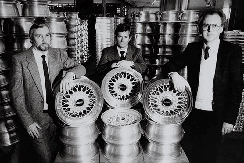 black and white photo of three men standing next to stacks of wheels