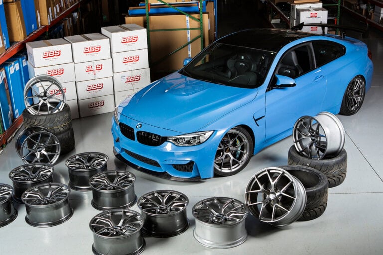 Light blue BMW m3 parked in a warehouse with wheels laying all around it