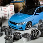 Light blue BMW m3 parked in a warehouse with wheels laying all around it