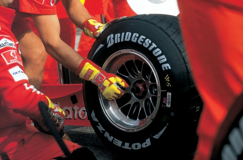 Man with yellow and red gloves holding onto a race car wheel with BBS wheels and Bridgestone tires