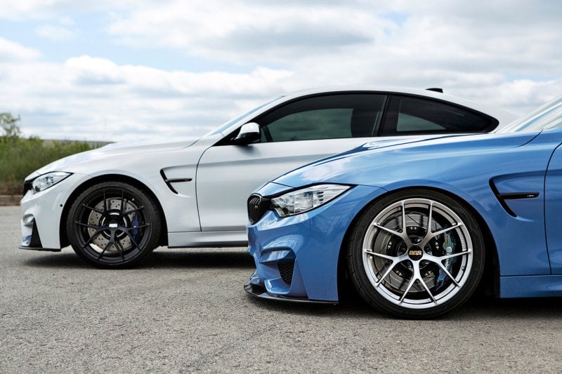 A white car parked behind a blue bmw, both with BBS wheels