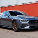 Grey 2024 Mustang GT driving past red shipping containers