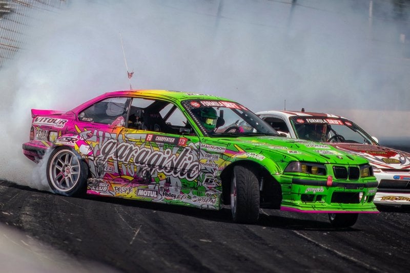 Pink and green BMW E36 drifting through a turn with stickers all along the side of the car