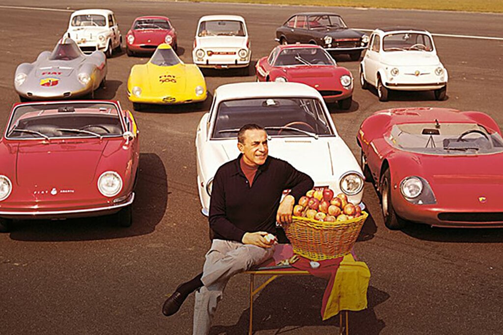 man sitting on a chair infront of a bunch of vehicles from red, to white, to yellow