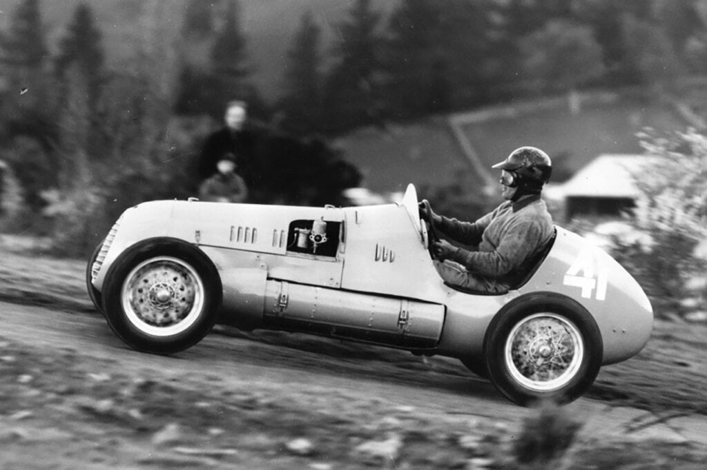 black and white photo of a man with a helmet sitting in a silver race car