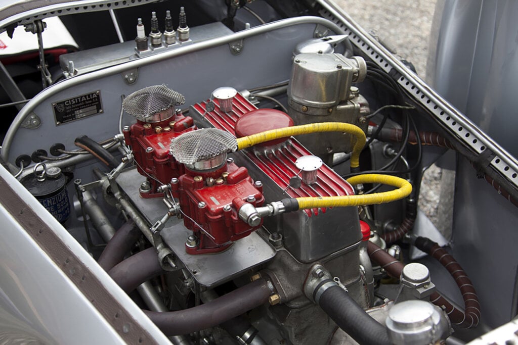 small engine of a silver car with a red valve cover with yellow hoses on top