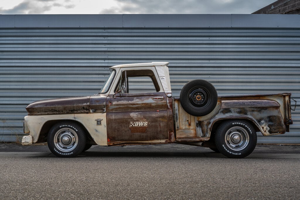 side shot of a rusted C10 with a spare tire on the side of the bed along a striped wall