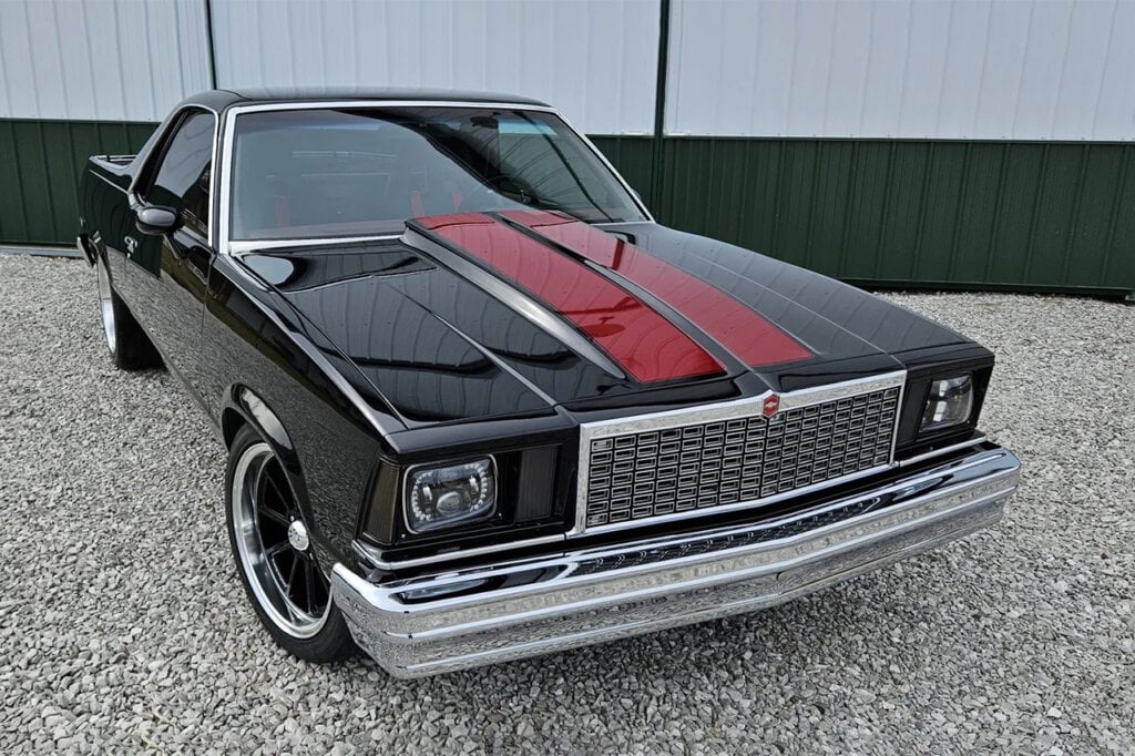 Black El Camino with red racing stripes parked on a gravel road