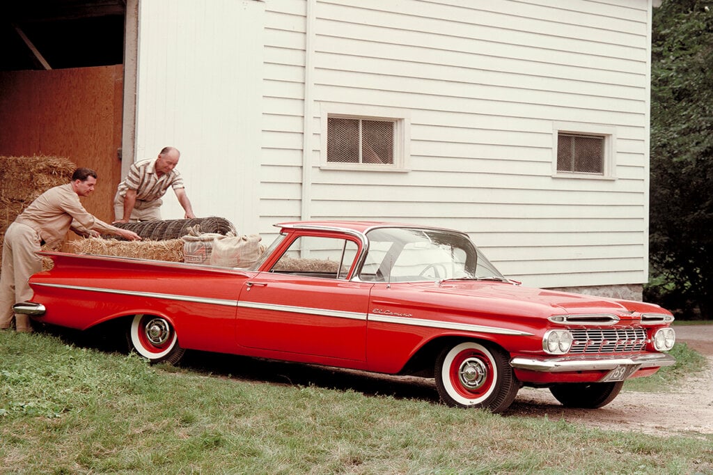 Two men loading up hay in the bed of a red car