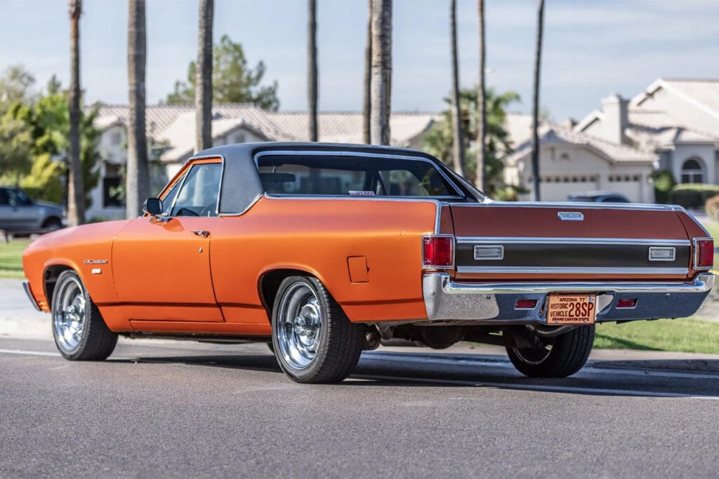 Orange El Camino parked near sidewalk with palm trees in background