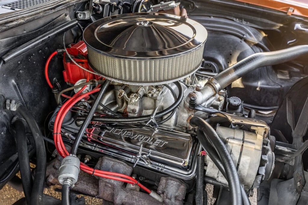 Engine block of a muscle car with a carburetor on top and red hoses