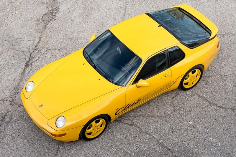 Yellow Porsche 968 parked on the ground with cracks on it