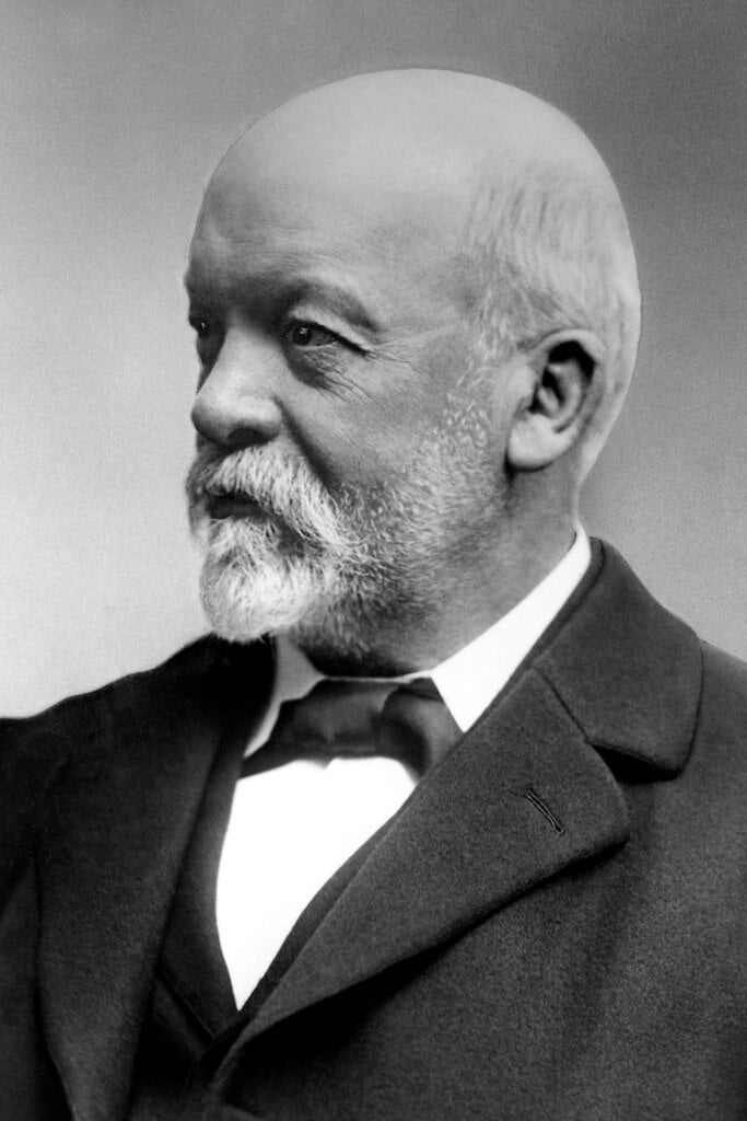 black and white image of a bald man with white mustache and beard with a suit on looking to his right