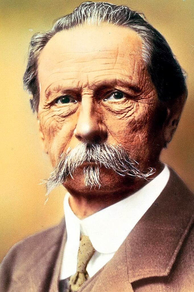 colored image of a man with grey mustache with a brown suit
