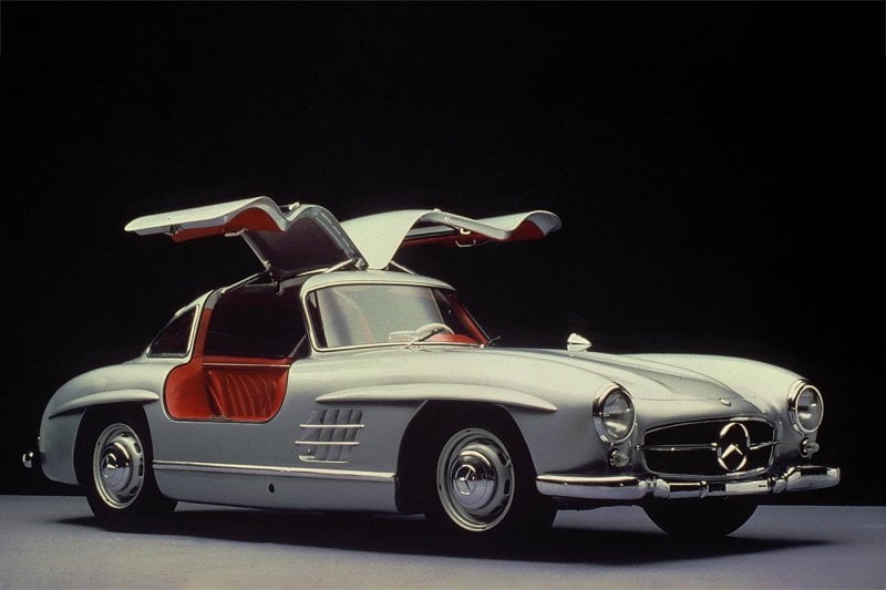 Silver 300SL with red interior and gull wing doors open on black background
