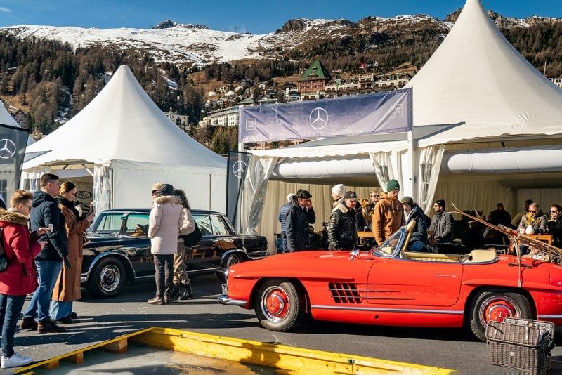 Black 600 and red 300SL Mercedes vehicles parked near tents and people