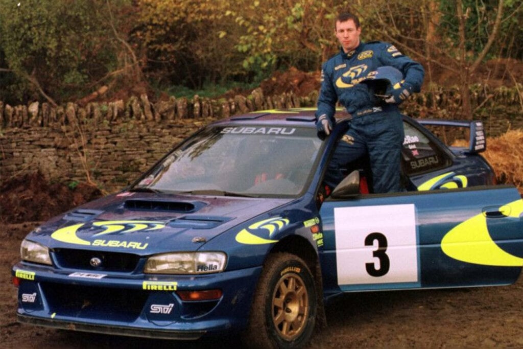 blue Subaru WRX with a man in a race suit standing next to it