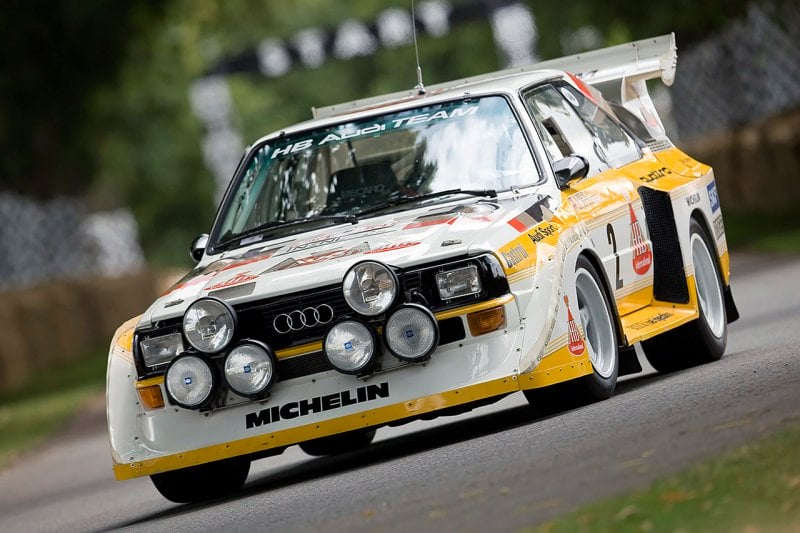 Yellow and white Audi Quattro pictured at an angle with grass and trees behind it