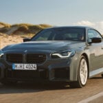Grey BMW M2 driving down the freeway with sand and grass hills behind it