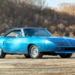 Blue Plymouth Superbird parked on dirt road with trees in background