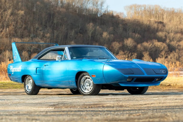 Blue Plymouth Superbird parked on dirt road with trees in background