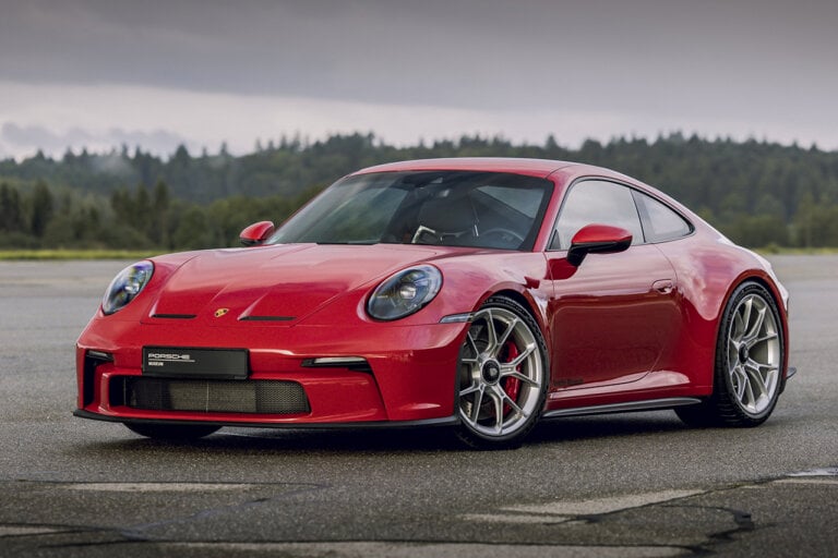red Porsche 911 992 parked on asphalt with trees and cloudy sky in background