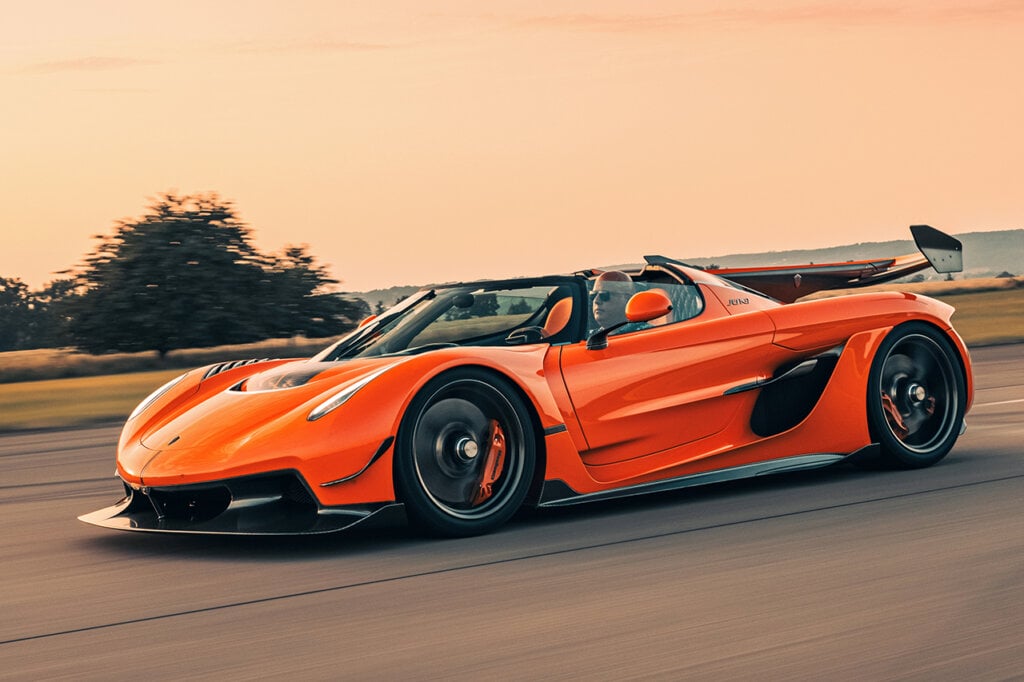 man with glasses driving an orange Koenigsegg Jesko attack with sunset in background